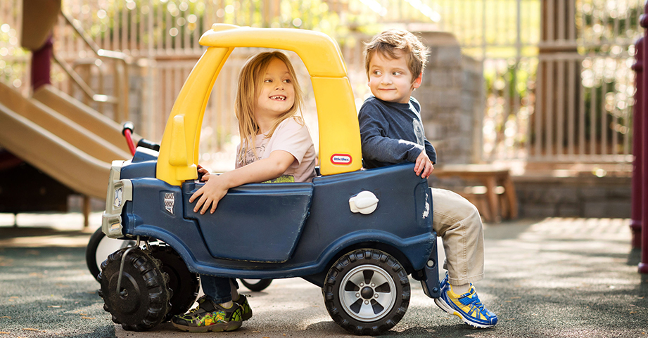 Boy and girl riding in car on playground at preschool